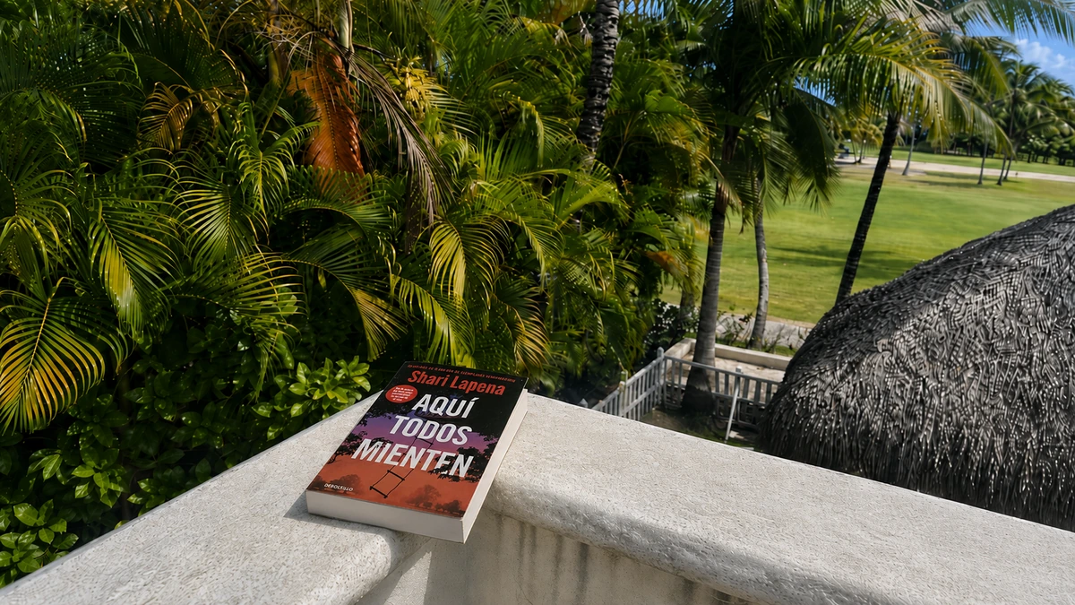 Libro Aquí todos mienten, de Shari Lapena, sobre una balaustrada blanca con palmeras tropicales al fondo.