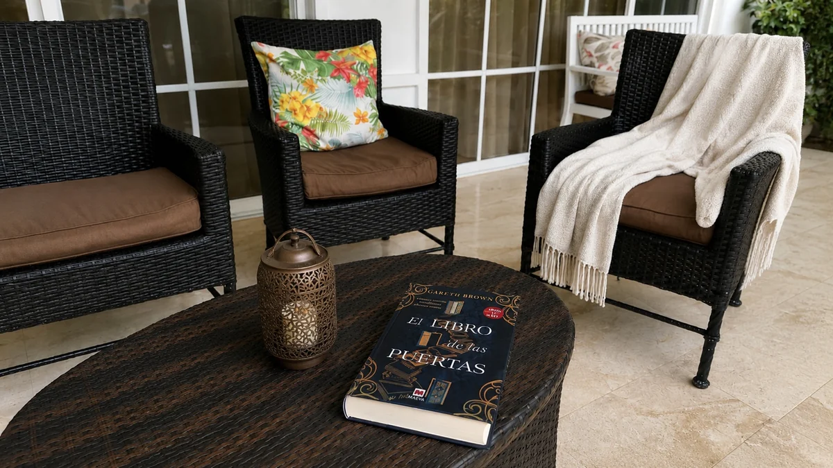Libro El libro de las puertas sobre una mesa de mimbre en un porche con sillones negros y una manta clara.