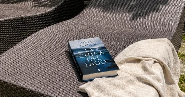 Libro La chica del lago sobre una hamaca junto a unas toallas y un refresco.