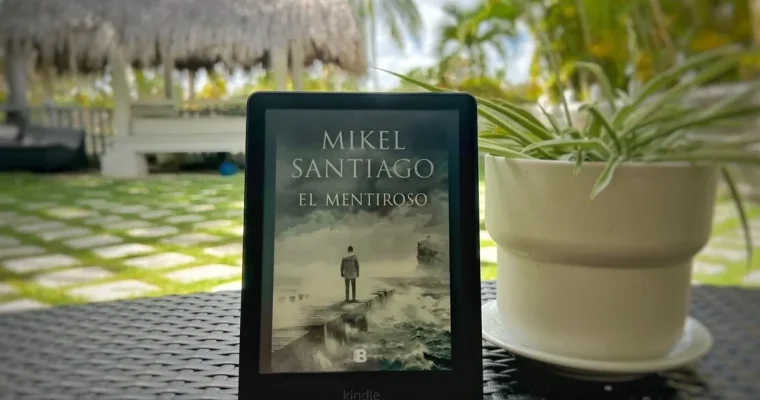 Kindle con la portada de El mentiroso, de Mikel Santiago, sobre una mesa junto a una planta.