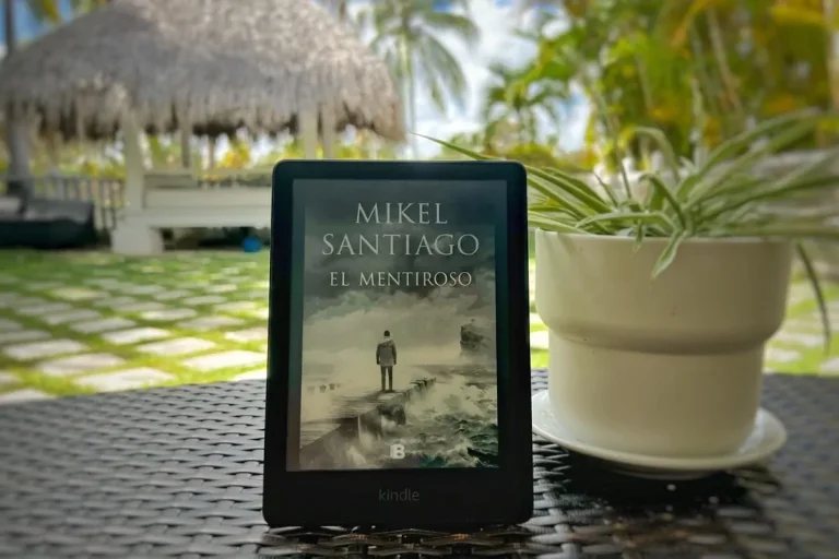 Kindle con la portada de El mentiroso, de Mikel Santiago, sobre una mesa junto a una planta.